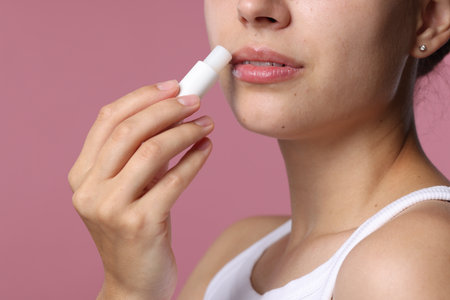 Young woman with lip balm on pink background, closeupの写真素材