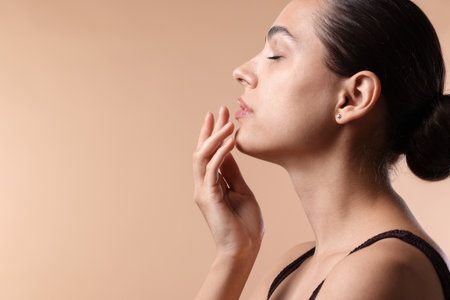 Young woman with lip balm on beige background, space for textの写真素材