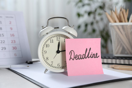 Sticky note with word Deadline, alarm clock, stationery and calendar on table indoors