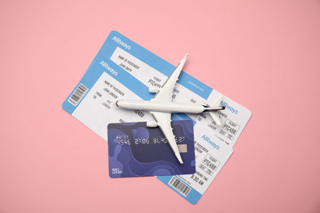 Airplane model, tickets and credit card on pink background, top view
