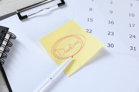 Sticky note with word Deadline, clipboard, calendar, pen and notebook on table, closeup