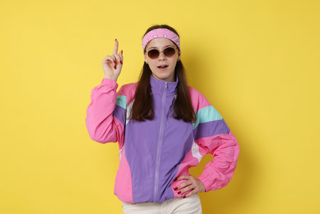 Teenage girl in sunglasses pointing at something on yellow backgroundの写真素材