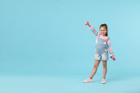 Little girl with dumbbells on light blue background, space for textの写真素材