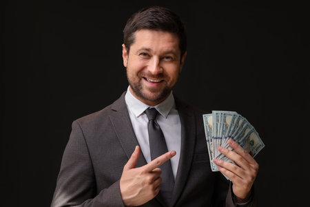 Happy banker pointing at dollar banknotes on black background