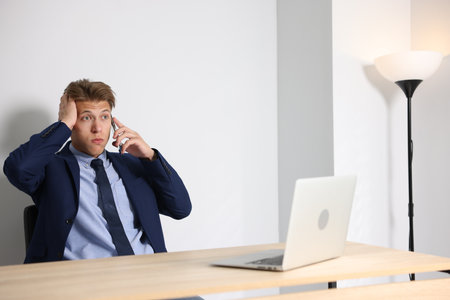 Young businessman with laptop complaining to someone via phone at wooden table indoorsの写真素材