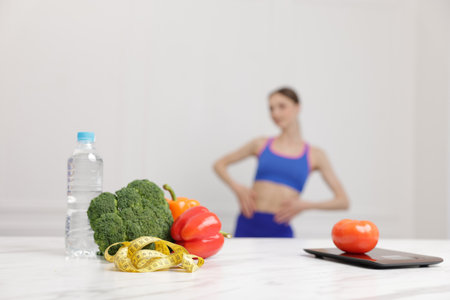 Slim woman posing indoors, focus on vegetables, measuring tape, water and kitchen scaleの写真素材