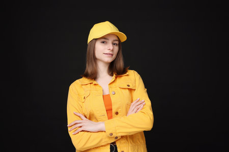 Young woman wearing stylish yellow baseball hat on black backgroundの写真素材
