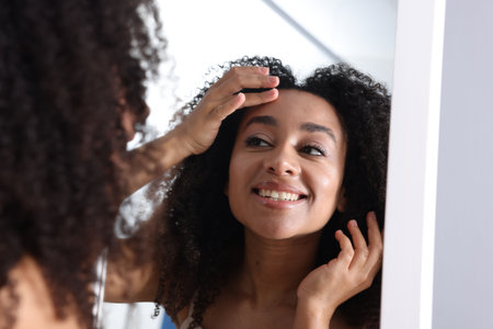 Beautiful Brazilian woman with healthy skin looking at mirror indoorsの写真素材