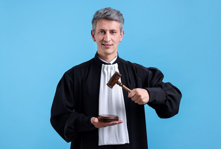 Smiling judge with mallet and sound block on light blue backgroundの写真素材