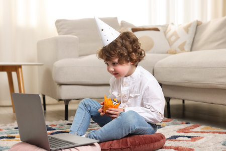 Birthday celebration. Little boy with cupcake having video call via laptop at homeの写真素材