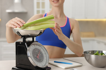 Woman weighting celery on kitchen scale at white table indoors, closeupの写真素材