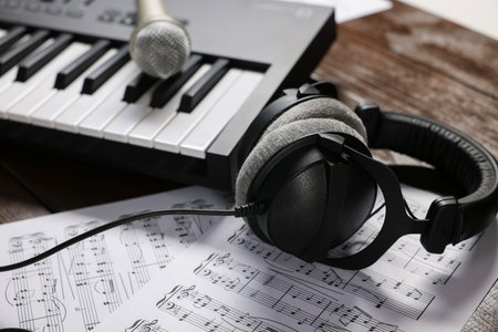 MIDI keyboard, headphones, microphone and music sheets on wooden table, closeupの写真素材