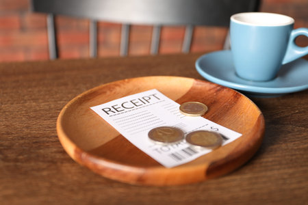Tips, receipt and cup of drink on wooden table in cafe, closeup