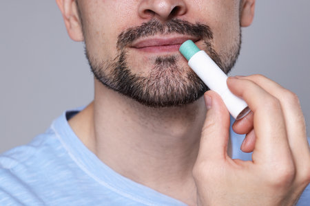 Man applying lip balm onto his lips on grey background, closeupの写真素材