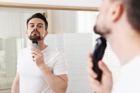 Handsome man shaving with trimmer near mirror at homeの写真素材