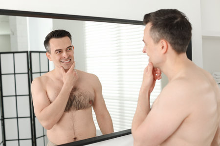 Smiling man after shaving looking at mirror in bathroomの写真素材