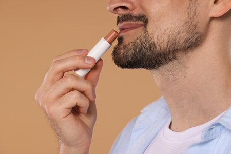 Man applying lip balm onto his lips on light brown background, closeupの写真素材
