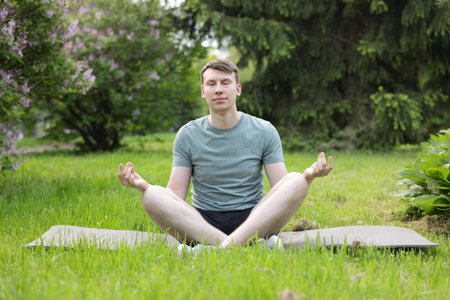 Young man practicing yoga on mat in parkの写真素材