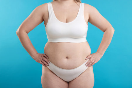 Weight loss. Plus size woman in underwear on light blue background, closeupの写真素材