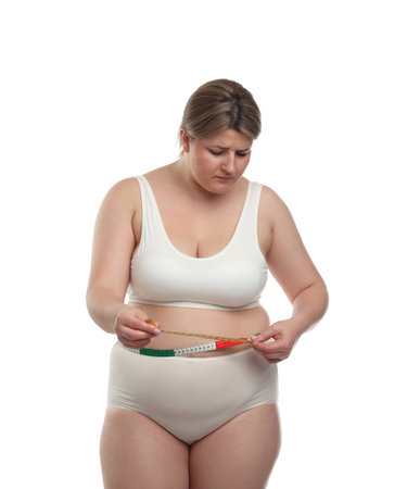 Weight loss. Plus size woman measuring waist with tape on white backgroundの写真素材