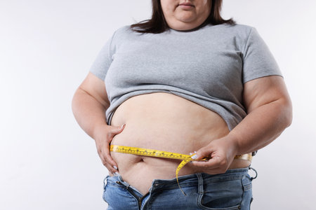 Overweight woman measuring her belly with tape on white background, closeupの写真素材