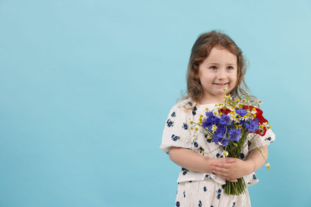 Cute little girl with bouquet of beautiful flowers on light blue background, space for text