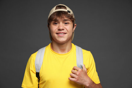 Portrait of smiling teenage boy in baseball hat on grey background