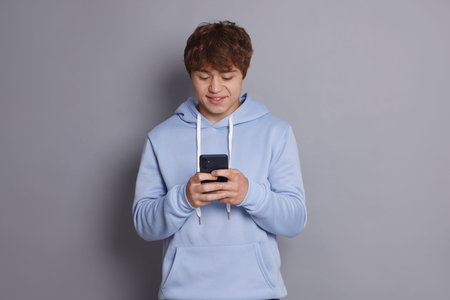Smiling teenage boy using smartphone on grey backgroundの写真素材