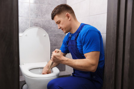 Plumber unclogging toilet with hand plunger indoorsの写真素材