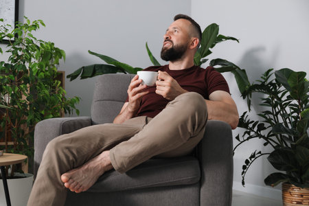 Harmony. Man with cup of drink in armchair at homeの写真素材
