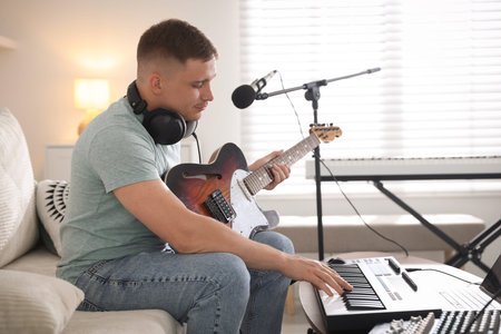 Man working with guitar and MIDI keyboard on sofa in home studio