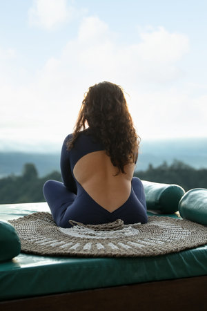 Woman meditating on mat in mountains, back view