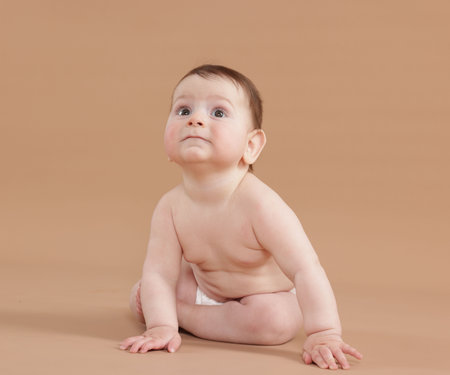 Cute little baby in diaper sitting on beige backgroundの写真素材