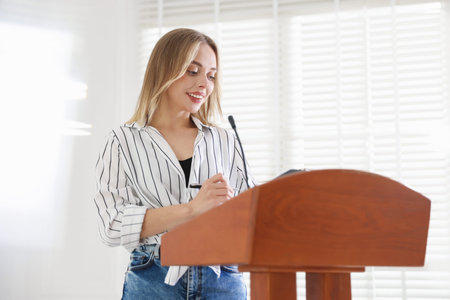 Woman giving public speech with microphone at lectern indoorsの写真素材