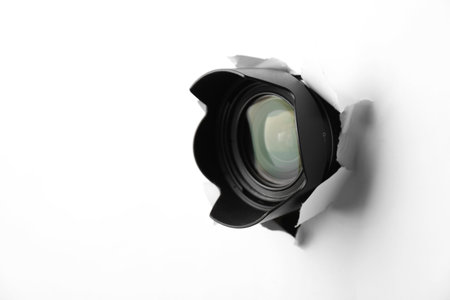 Hidden camera lens through torn hole in white paper. Space for textの写真素材
