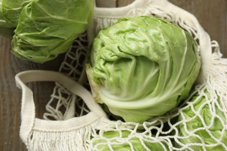 Fresh cabbages and net bag on wooden table, closeup