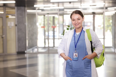 Medical student in uniform with backpack indoors, space for text