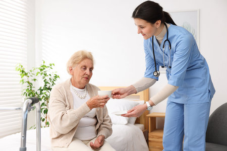 Nurse giving cup of drink to senior woman indoors. Home health care service