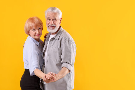 Lovely senior couple together on yellow background, space for text