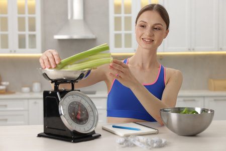 Woman weighting celery on kitchen scale at white table indoorsの写真素材