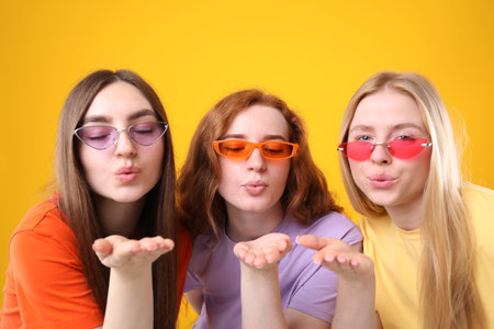 Beautiful women with different hair colors blowing kisses on orange background