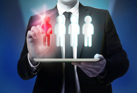 Dismissal. Businessman choosing human figure on virtual screen above tablet computer against dark blue background, closeupの写真素材