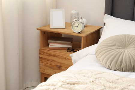Bedside table with alarm clock and decor near bed indoors