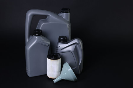 Motor oil in plastic canisters, filter and funnel on black background, space for text