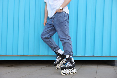 Man with roller skates near light blue wall outdoors, closeup