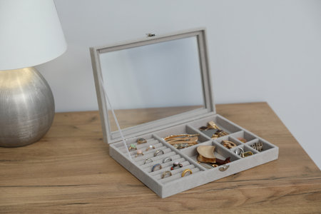 Jewelry box with many different accessories and lamp on wooden table near white wall indoors, closeupの写真素材