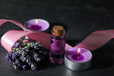 Bottle of lavender essential oil, flowers, burning candles and ribbon on black table, closeupの写真素材