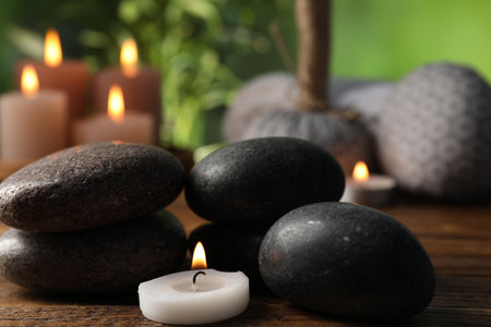 Spa composition with stones and burning candle on wooden table against blurred green background, closeupの写真素材