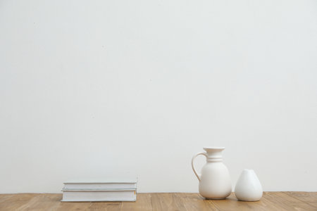 Different vases and books on wooden table near white wall indoorsの写真素材