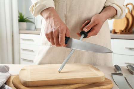Man sharpening knife with sharpener at beige table indoors, closeupの写真素材